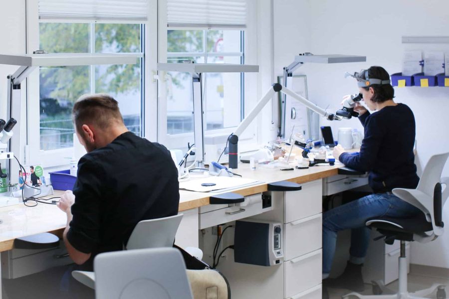 Mitarbeiter eines Zahnlabors bei der Arbeit mit Mikroskop und weiteren Werkzeugen