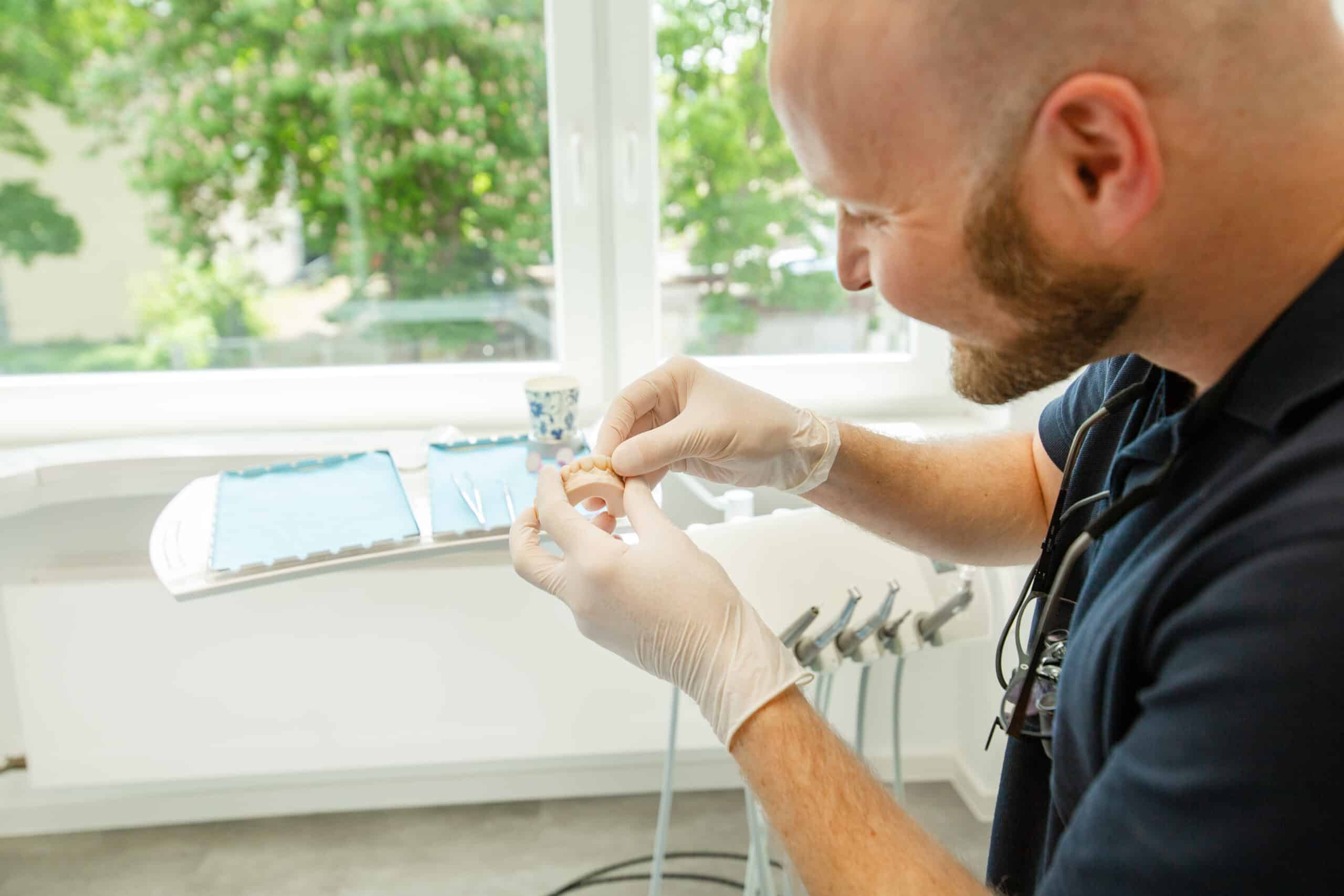 Ein Zahnarzt unserer Praxis mit einem Zahnersatz in der Hand